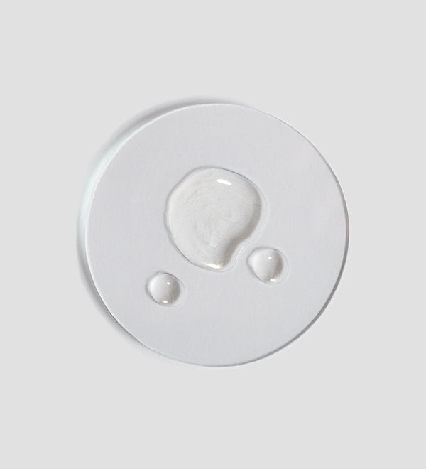 Clear liquid droplets on a white surface showcasing the texture of Tranquillity Oil (Bath & Body) | [ comfort zone ] for skincare and body care wellness.