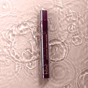 UltraVolume Tubing Mascara - Black | Blinc tube submerged in rippling water with soft pink lighting, highlighting a waterproof makeup product.