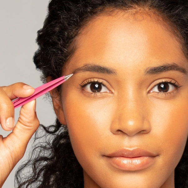 Woman holding Pretty In Pink Point Tweezer | Tweezerman near her eyebrow, demonstrating precision grooming tool for skincare and wellness care.