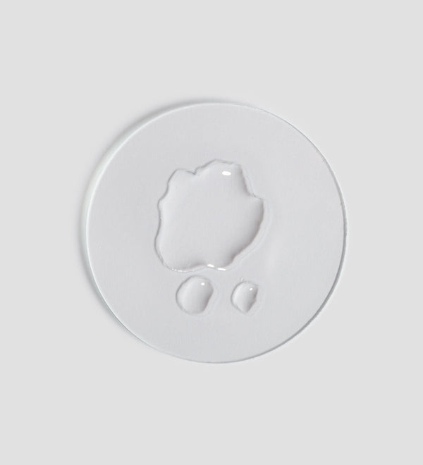 Clear liquid drops on a white surface demonstrating the texture of Remedy Toner | [ comfort zone ], highlighting its lightweight and hydrating skincare formula.