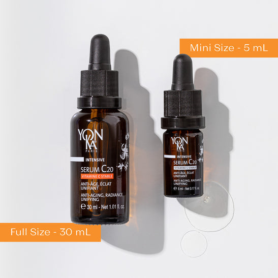 Two amber glass dropper bottles of Serum C20 | Yon-Ka Paris in 30 mL full size and 5 mL mini size with some serum drops next to them on a white background, highlighting anti-aging skincare.