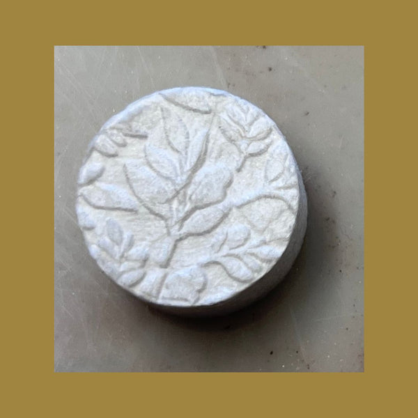 Round white solid makeup remover tablet with embossed botanical leaf design, representing natural skincare ingredients for Make Up Remover Wipes | Functional Botanicals.