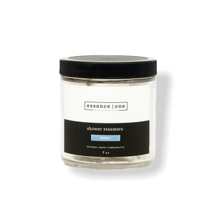Clear glass jar with black lid containing Shower Steamer | Essence One, labeled as energy with a natural, safe, and therapeutic formula for wellness and body care.
