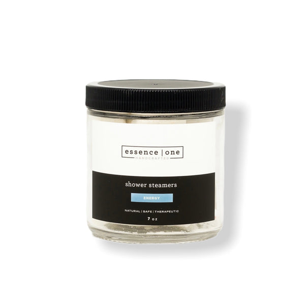 Clear glass jar with black lid containing Shower Steamer | Essence One, labeled as energy with a natural, safe, and therapeutic formula for wellness and body care.
