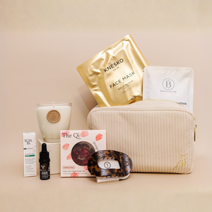 Luxe Bath Ritual Kit | Live Love Spa featuring a soft beige toiletry bag with gold zipper, skincare essentials including a gold face mask, white sachet, scented candle, facial serum, tea, and a tortoiseshell facial massage tool.