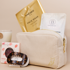 Luxe Bath Ritual Kit | Live Love Spa featuring a beige textured zippered pouch with skincare and body care items including a gold face mask, bath soak sachet, herbal tea, and a tortoiseshell recovery tool.