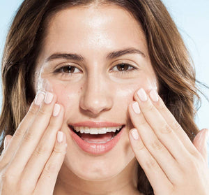 Close-up of a smiling woman gently applying Kale Water Weightless Moisturizer | Farmhouse Fresh to her glowing skin, highlighting natural skincare and hydration.