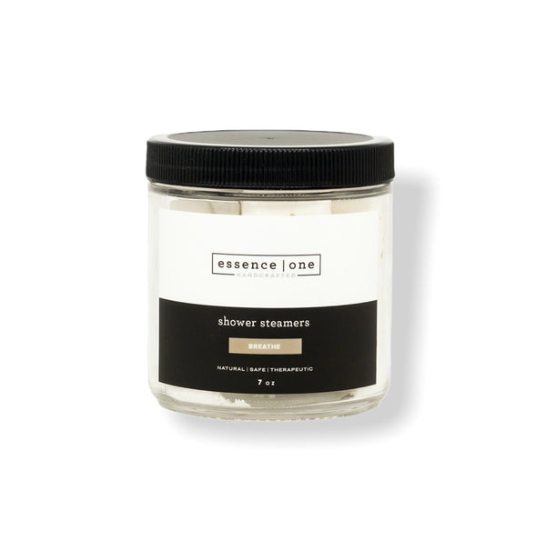 Clear glass jar with black lid containing shower steamers labeled "essence one" and "Breathe," part of the Shower Steamer | Essence One collection for wellness and body care.