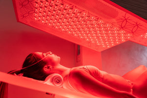 Woman lying under red light therapy panel with eyes closed, using Ammortal Chamber | Ammortal for wellness and recovery.