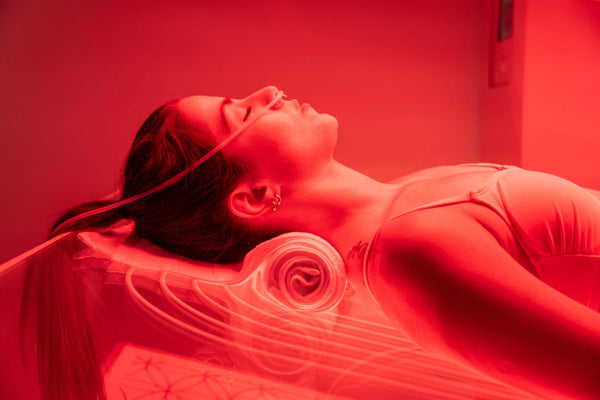 Woman relaxing with eyes closed inside a red-lit wellness device, using Ammortal Chamber | Ammortal for enhanced body care and recovery.