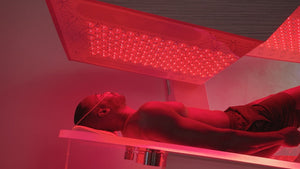 A person lying under red light therapy panels in a wellness setting, showcasing the Ammortal Chamber | Ammortal designed for recovery and body care.