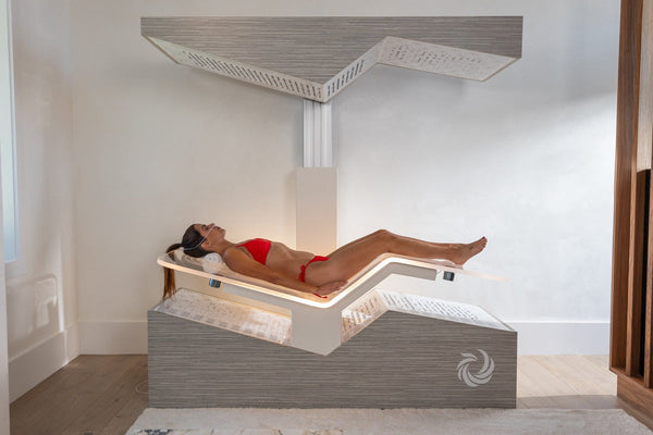A woman in a red bikini lying inside a modern wellness device called Ammortal Chamber | Ammortal, designed for relaxation and recovery in a minimalistic room.