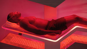 A man lying relaxed inside a red-lit wellness pod designed for recovery and body care, featuring Ammortal Chamber | Ammortal technology.