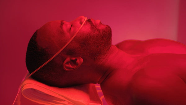 Man lying down with closed eyes under red light therapy treatment in a wellness setting using Ammortal Chamber | Ammortal for recovery and relaxation.