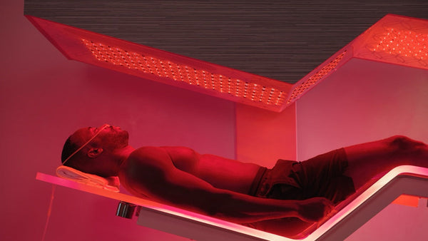 A man relaxing under red LED light therapy panels on a modern wellness device designed for skincare and recovery, featuring the Ammortal Chamber | Ammortal.