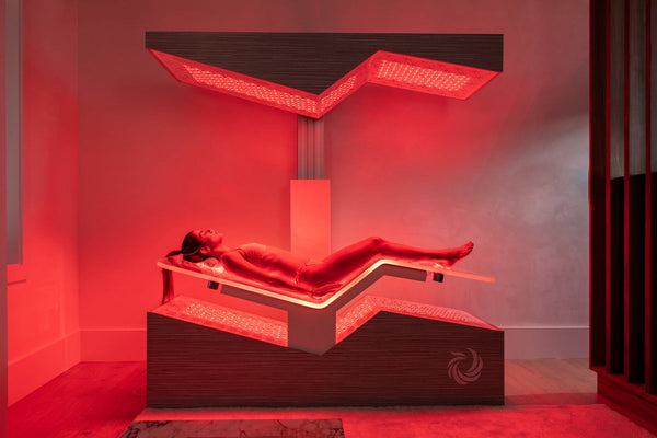 Woman lying inside a modern red light therapy wellness device emitting soothing red light for skincare and body care benefits, labeled Ammortal Chamber | Ammortal.