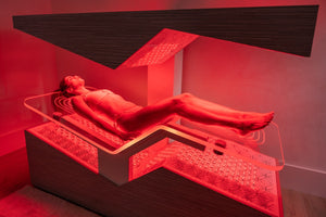 Woman relaxing inside a red-lit wellness device designed for skincare and recovery, featuring the Ammortal Chamber | Ammortal for body care and spa treatments.