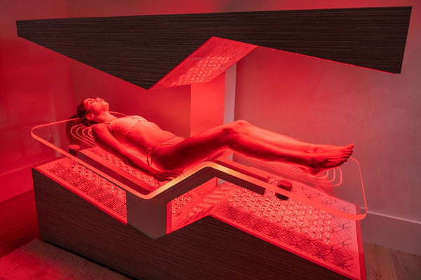 Woman relaxing inside a red-lit wellness device designed for skincare and recovery, featuring the Ammortal Chamber | Ammortal for body care and spa treatments.