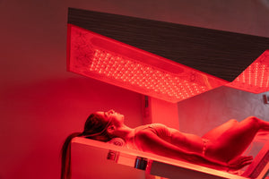 Woman relaxing under red light therapy panel inside Ammortal Chamber | Ammortal wellness device for recovery and skincare benefits.