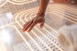 Close-up of a hand gently touching a sleek, illuminated surface with curved light patterns, showcasing the Ammortal Chamber | Ammortal wellness device designed for relaxation and recovery.