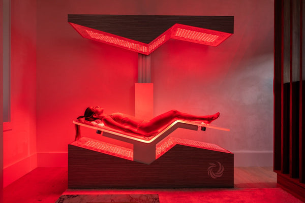 A person relaxing inside the Ammortal Chamber | Ammortal under red wellness light therapy panels in a modern spa setting.