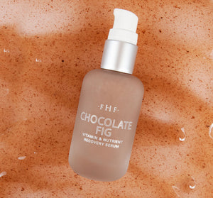 Bottle of Chocolate Fig Vitamin Recovery Serum | Farmhouse Fresh on a textured brown surface with water droplets, highlighting skincare and recovery benefits.