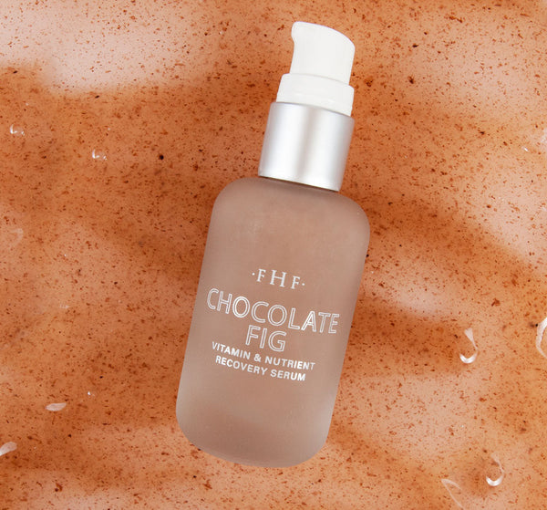 Bottle of Chocolate Fig Vitamin Recovery Serum | Farmhouse Fresh on a textured brown surface with water droplets, highlighting skincare and recovery benefits.