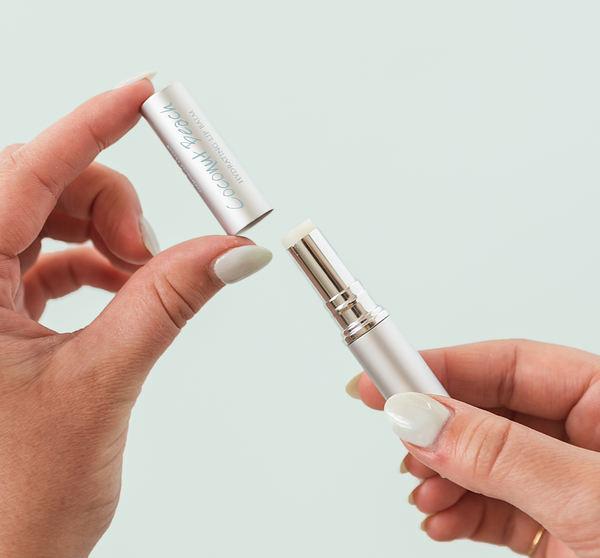 Hands holding an open tube of Coconut Beach® Hydrating Lip Balm | Farmhouse Fresh against a light background, showing the balm stick and cap with clean white nails.