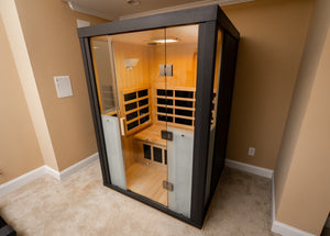 Modern infrared sauna cabin with wooden interior and glass door, designed for relaxation and wellness, featuring heating panels and ambient lighting, HaloSauna™ | Halotherapy Solutions.