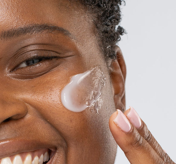 Close-up of a smiling person applying Kale Water Weightless Moisturizer | Farmhouse Fresh to their cheek, demonstrating skincare routine with smooth, hydrated skin.