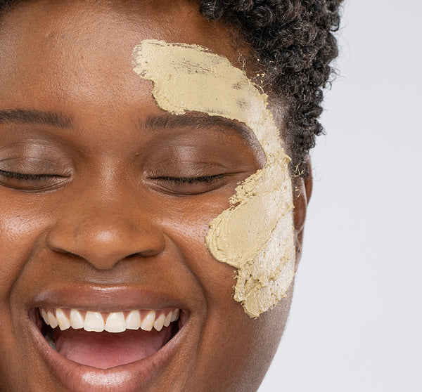 Close-up of a smiling person with eyes closed applying Matcha Purity™ Calm & Clear Purification Mask | FarmHouse Fresh on their cheek, showcasing skincare and wellness.