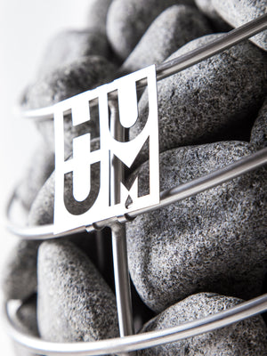 Close-up of smooth sauna stones held in a metal basket with a decorative cutout, part of the E7G Barrel Sauna - 4-6 Person | Western Sol, highlighting quality materials for wellness and relaxation.
