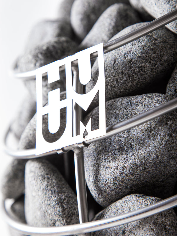Close-up of smooth sauna stones held in a metal basket with a decorative cutout, part of the E7G Barrel Sauna - 4-6 Person | Western Sol, highlighting quality materials for wellness and relaxation.