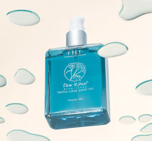 Clear blue bottle of Dew Ritual® Triple Lipid Body Oil | Farmhouse Fresh with white pump dispenser surrounded by scattered drops of oil on a light background for skincare and body care wellness.