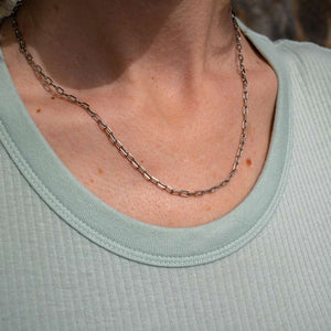 Close-up of a person wearing a silver tone chain necklace with elongated links paired with a light green ribbed top, featuring Frolic Paperclip Necklace /silver tone | Purpose Jewelry.