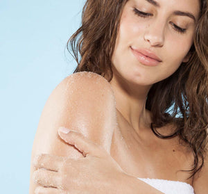Woman gently exfoliating her shoulder with a sugar scrub, demonstrating the skincare benefits of the Honey I’m Smooth Limited Edition Set | Farmhouse Fresh.