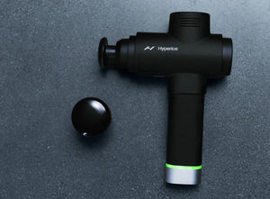 Heated Head Attachment | Hyperice shown with a black percussion massage device on a dark surface, highlighting wellness recovery tools for muscle relaxation.