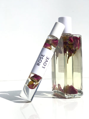 Rose Love Organic Perfume Roll-on | Hydra Bloom featuring clear glass bottles containing a light liquid with suspended rosebuds, showcased on a white surface with natural light.