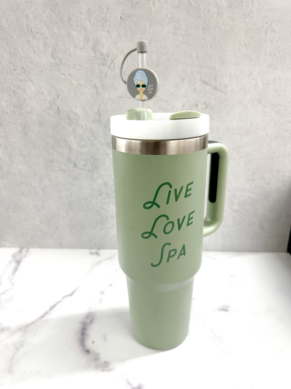 A pale green travel tumbler with a handle, featuring the words "Live Love Spa" in elegant green script and a straw topped with the Spa Girl Straw Topper | Live Love Spa accessory.