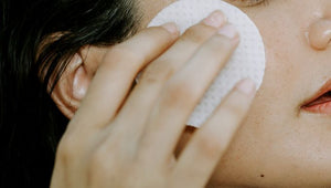 Close-up of a person gently applying an Instant Perfection Peel Pads | Skin Authority skincare pad to their cheek for a refreshing facial treatment.