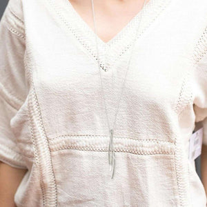 Close-up of a person wearing a delicate silver pendant on a slim chain paired with a textured cream top, showcasing the elegant Kailani Necklace | Purpose Jewelry.