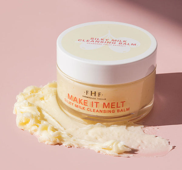 Make it Melt Silky Milk Cleansing Balm | Farmhouse Fresh in a clear jar with a white lid, creamy balm texture smeared on a pink surface, showcasing skincare wellness product.