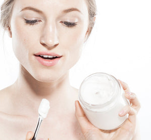 Woman holding an open jar of Moon Dip Back To Youth Ageless Body Mousse | Farmhouse Fresh while scooping the white creamy body care product with a spatula.