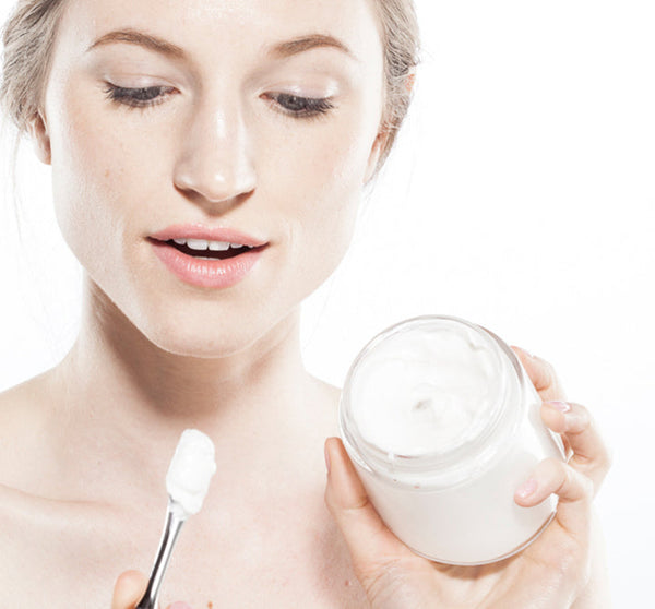 Woman holding an open jar of Moon Dip Back To Youth Ageless Body Mousse | Farmhouse Fresh while scooping the white creamy body care product with a spatula.
