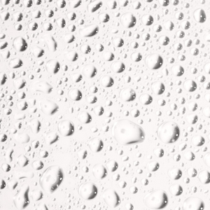 Close-up of clear water droplets on a smooth surface illustrating hydration and freshness related to Face Tan Water - Dark | NUDA skincare.