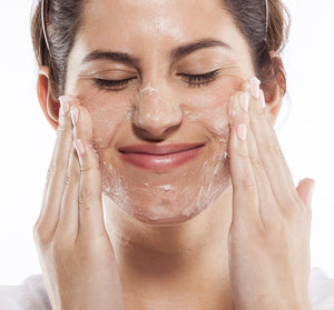 Woman gently applying One Fine Day Flawless Face Polish | Farmhouse Fresh exfoliating skincare product to her face with closed eyes, smiling softly.
