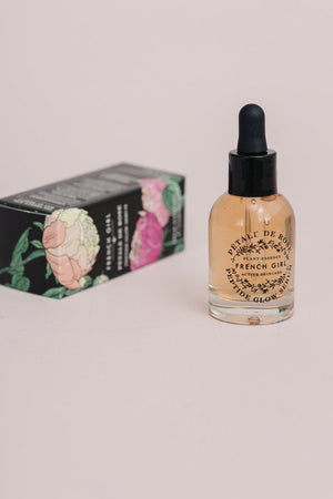 Clear glass dropper bottle of Peptide Glow Serum | French Girl with light amber liquid, standing beside a black box decorated with colorful floral illustrations for skincare use.