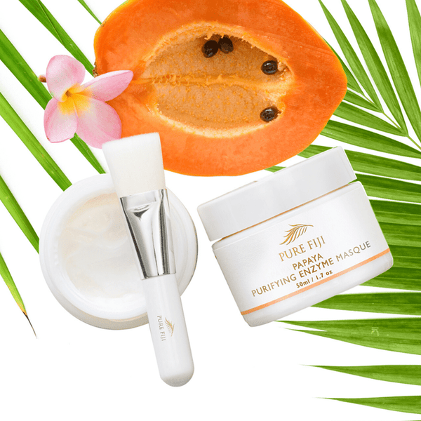 Papaya Purifying Enzyme Masque | Pure Fiji with creamy masque, application brush, fresh papaya half, tropical flower, and palm leaf for skincare and wellness.