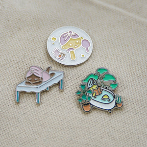 Three colorful enamel pins featuring spa and wellness themes including facial care, relaxation on a massage table, and a cozy bathtub surrounded by plants, showcasing the Fab Spa Life Enamel Pin - Limited Edition | Lucky Owl.