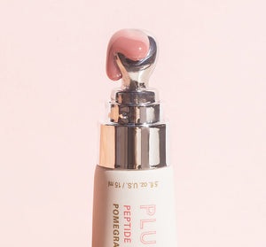 Close-up of a silver-tipped applicator releasing a soft pink balm from Plump Up Pretty Peptide Lip Treatment | Farmhouse Fresh against a pale pink background.
